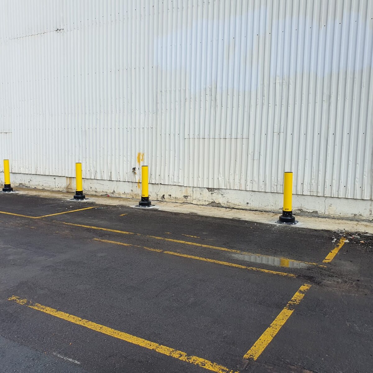Professionally installed yellow safety bollards protecting a commercial building in a car park.